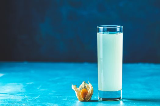 Alcoholic cocktail with Ouzo greek anise brandy or Arabic alcohol drink Raki in highball glass, decorated Physalis peruviana and brown sugar on blue concrete surface.