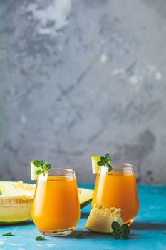 Yellow orange cocktail with melon and mint in glass on blue concrete background, close up. Summer drinks and alcoholic cocktails. Alcoholic or detox cocktail