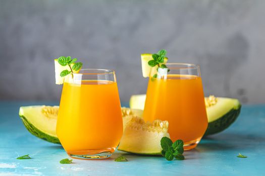 Yellow orange cocktail with melon and mint in glass on blue concrete background, close up. Summer drinks and alcoholic cocktails. Alcoholic or detox cocktail.