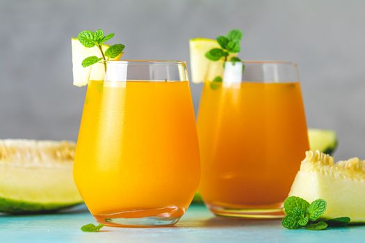 Yellow orange cocktail with melon and mint in glass on blue concrete background, close up. Summer drinks and alcoholic cocktails. Alcoholic or detox cocktail
