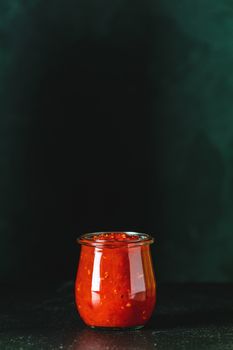 Homemade DIY natural canned hot tomato sauce chutney with chilli or adjika in glass jar standing on wooden table, selective focus, copy space for you text