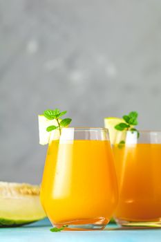 Yellow orange cocktail with melon and mint in glass on blue concrete background, close up. Summer drinks and alcoholic cocktails. Alcoholic or detox cocktail