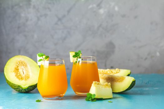 Yellow orange cocktail with melon and mint in glass on blue concrete background, close up. Summer drinks and alcoholic cocktails. Alcoholic or detox cocktail