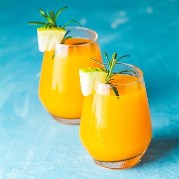 Yellow orange cocktail with melon and mint in glass on blue concrete background, close up. Summer drinks and alcoholic cocktails. Alcoholic or detox cocktail