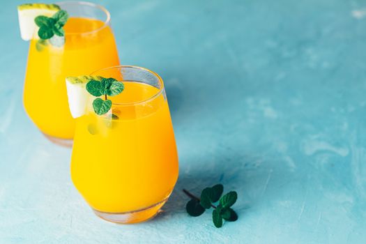 Yellow orange cocktail with melon and mint in glass on blue concrete background, close up. Summer drinks and alcoholic cocktails. Alcoholic or detox cocktail.