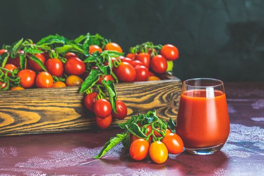 Glass of fresh delicious jummy red tomato juice and fresh tomatoes in wooden box. Dark background. Close up. Gmo free. Natural good food