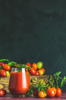 Glass of fresh delicious jummy red tomato juice and fresh tomatoes in wooden box. Dark background. Close up. Gmo free. Natural good food