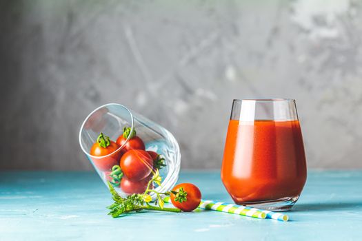 Glasses of fresh delicious jummy red tomato juice and fresh raw tomatoes with pink salt in spoon on light concrete surface. Close up. Gmo free. Natural good food.