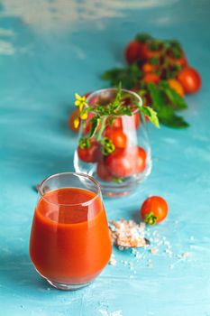 Glasses of fresh delicious jummy red tomato juice and fresh raw tomatoes with pink salt in spoon on light concrete surface. Close up. Gmo free. Natural good food.