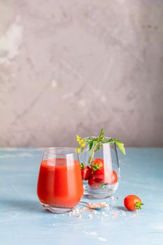 Glasses of fresh delicious jummy red tomato juice and fresh raw tomatoes with pink salt in spoon on light concrete surface. Close up. Gmo free. Natural good food.