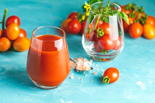 Glasses of fresh delicious jummy red tomato juice and fresh raw tomatoes with pink salt in spoon on light concrete surface. Close up. Gmo free. Natural good food.