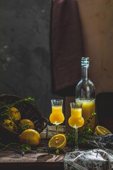 Limoncello in grappas wineglass with water drops and lavender on dark wooden table. Artistic still life on dark background with sunny light.