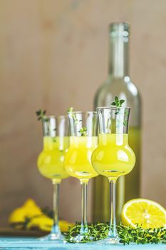 Limoncello with thyme in grappas wineglass with water drops on light concrete table. Artistic still life on light background with sunny light.