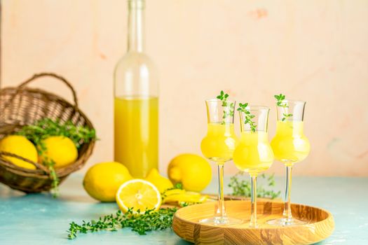 Limoncello with thyme in grappas wineglass with water drops on light concrete table. Artistic still life on light background with sunny light.
