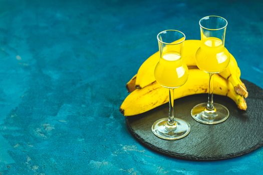 Banana flavoured liqueurs, which French call creme de banana, in  grappas wineglass on dark blue concrete surface. European aperitif drink. Selective focus, shallow depth of the fields, copy space.