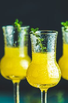 Limoncello with thyme in three grappas wineglass with water drops close up on dark background, shallow depth of the field.