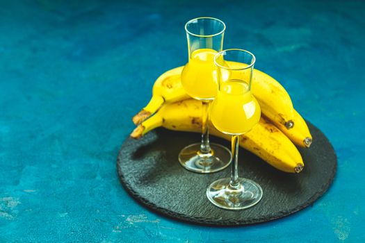 Banana flavoured liqueurs, which French call creme de banana, in  grappas wineglass on dark blue concrete surface. European aperitif drink. Selective focus, shallow depth of the fields, copy space.
