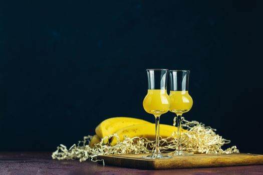 Banana flavoured liqueurs, which French call creme de banana, in  grappas wineglass on dark concrete surface. European aperitif drink. Selective focus, shallow depth of the fields, copy space.