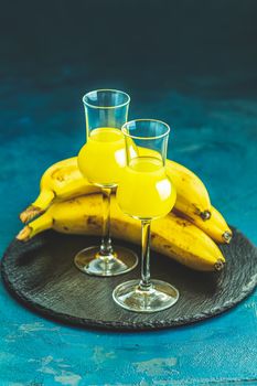 Banana flavoured liqueurs, which French call creme de banana, in  grappas wineglass on dark blue concrete surface. European aperitif drink. Selective focus, shallow depth of the fields, copy space.