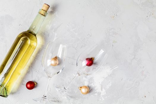 Creative food art background. Bottle of wine and two wineglasses with red and gold сhristmas balls on light gray concrete surface, top view, flat lay, copy space for you text.
