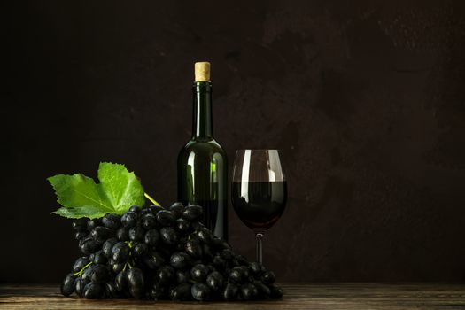Glasses and bottles of wine and grapes on dark claret bordeaux concrete surface background.