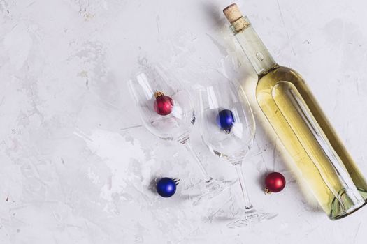 Creative food art background. Bottle of wine and two wineglasses with red and blue сhristmas balls on light gray concrete surface, top view, flat lay, copy space for you text.
