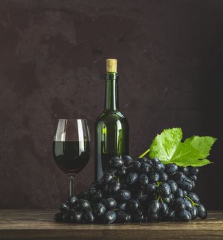 Glasses and bottles of wine and grapes on dark claret bordeaux concrete surface background