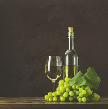 Glasses and bottles of wine and grapes on dark claret bordeaux concrete surface background.