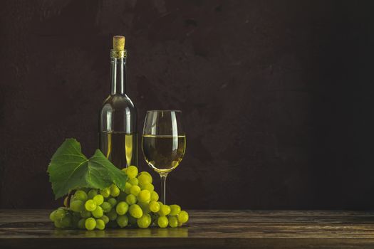Glasses and bottles of white wine and grapes on dark claret bordeaux concrete surface background	