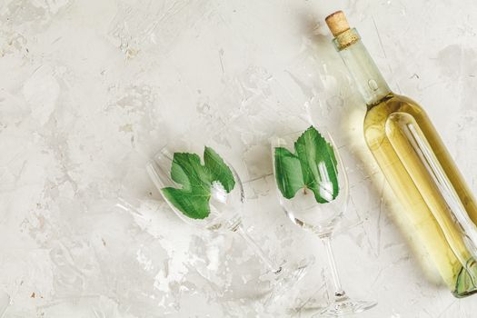 Creative food art background. Bottle of wine and two wineglasses with green grape leaves on light gray concrete surface, top view, flat lay, copy space for you text.