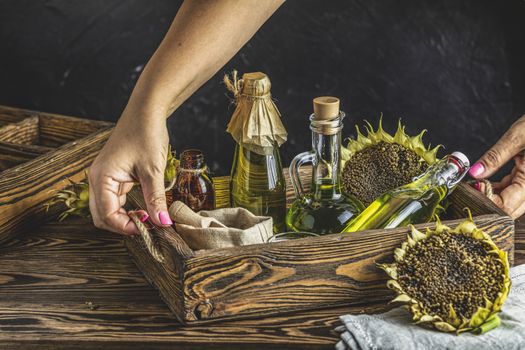 Female woman hands holding a tray with organic sunflower oil in a small glass jars with sunflower seeds. Closeup photo of sunflower oil with seeds on wooden background. Bio and organic product concept.