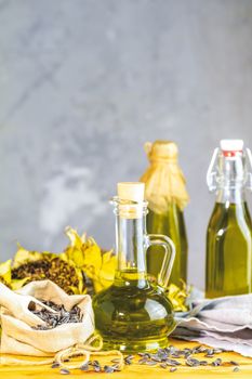 Various types of oil in bottles, dried sunflowers and seeds on wooden table. Close up, copy space.