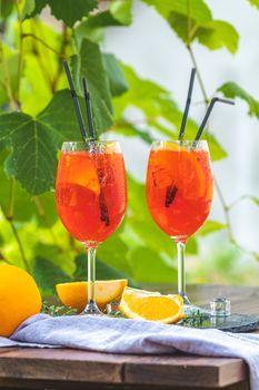 Two Aperol spritz cocktail in big wine glass with oranges, summer Italian fresh alcohol cold drink. Sunny garden with vineyard background.