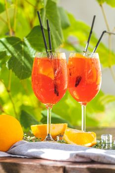 Two Aperol spritz cocktail in big wine glass with oranges, summer Italian fresh alcohol cold drink. Sunny garden with vineyard background, summer mood concept, selective focus