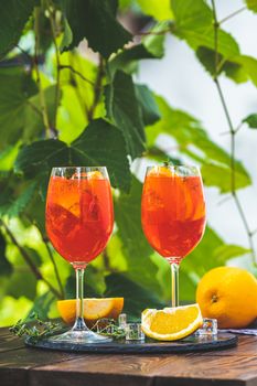 Two Aperol spritz cocktail in big wine glass with oranges, summer Italian fresh alcohol cold drink. Sunny garden with vineyard background, summer mood concept, selective focus