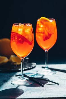 Two Aperol spritz cocktail in big wine glass with oranges, summer Italian fresh alcohol cold drink. Dark bar counter background with tools, summer mood concept, selective focus