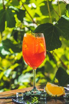 Aperol spritz cocktail in big wine glass with oranges, summer Italian fresh alcohol cold drink. Sunny garden with vineyard background, summer mood concept, selective focus