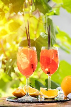 Two Aperol spritz cocktail in big wine glass with oranges, summer Italian fresh alcohol cold drink. Sunny garden with vineyard background, summer mood concept, selective focus