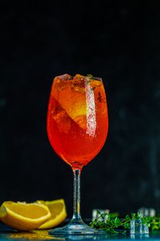 Cocktail aperol spritz in big wine glass with water drops on dark background. Summer alcohol cocktail with orange slices. Italian cocktail aperol spritz on slate board. Trendy beverage.
