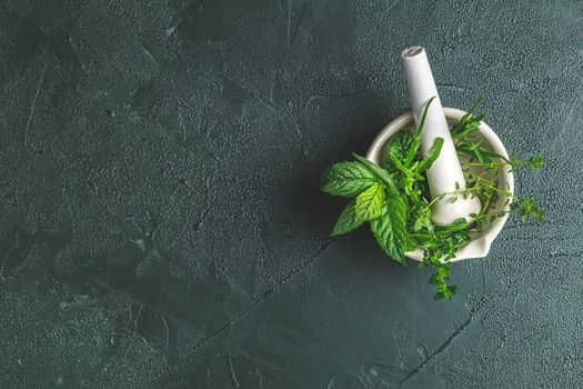 Mortar with  herbs and spices. Fresh herbs selection included rosemary, thyme, mint, lemon balm, parsley and arugula. Overhead view, copy space. Dark green concrete surface.