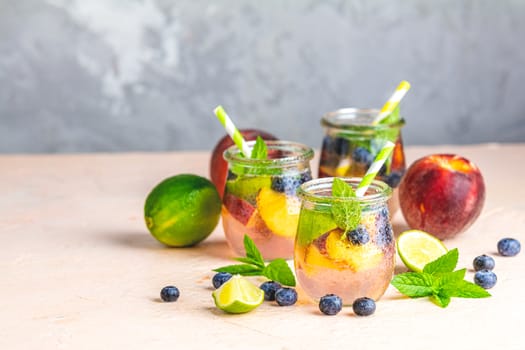 Blueberry and peach infused water, cocktail, lemonade or tea in jar with water drops. Summer iced cold drink with blueberry, lime, peach and mint