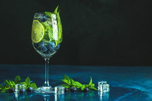 Summer alcoholic cocktail blueberry mojito with rum, mint, lime and ice, bar tools, dark background, selective focus, copy space