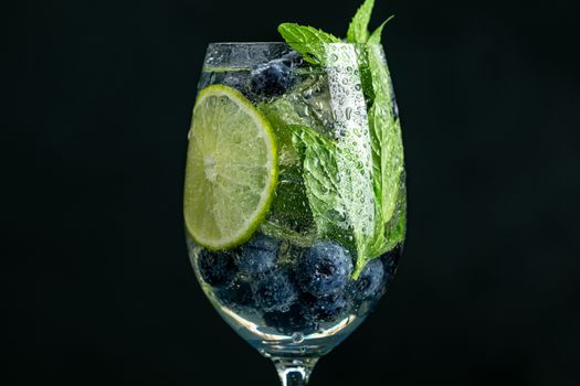 Summer alcoholic cocktail blueberry mojito with rum, mint, lime and ice, close up, dark background, selective focus, copy space