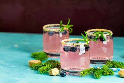 Fresh blueberry cocktail with rosemary and ice in glasses with decorate brown sugar on turquoise surface and black background. Christmas and New Year holiday welcome drink. 