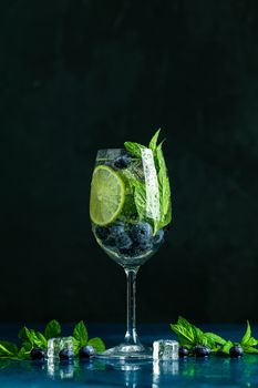 Summer alcoholic cocktail blueberry mojito with rum, mint, lime and ice, close up, dark background, selective focus, copy space