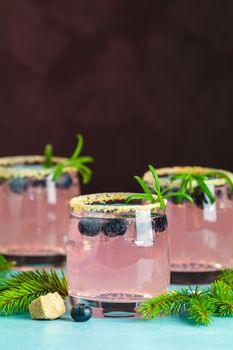 Fresh blueberry cocktail with rosemary and ice in glasses with decorate brown sugar on turquoise surface and black background. Christmas and New Year holiday welcome drink