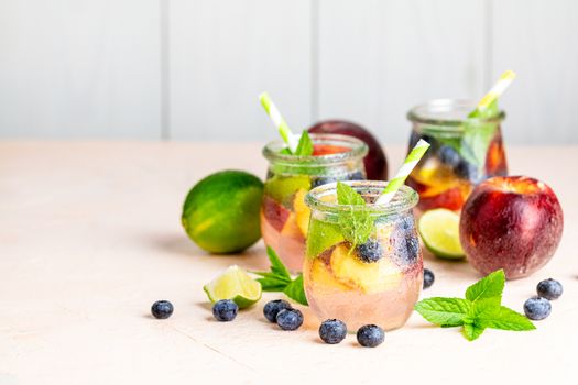 Blueberry and peach infused water, cocktail, lemonade or tea in jar with water drops. Summer iced cold drink with blueberry, lime, peach and mint