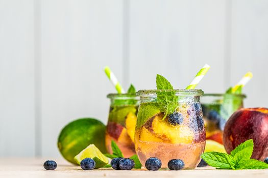 Blueberry and peach infused water, cocktail, lemonade or tea. Summer iced cold drink with blueberry, lime, peach and mint. Selective focus.