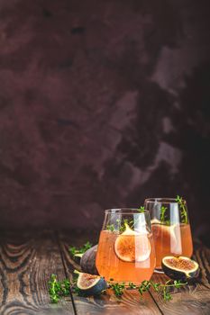 Pink cocktail with fig, thyme and ice in glass on dark wooden background, close up. Summer drinks and alcoholic cocktails. Alcoholic or detox cocktail