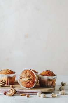 Vanilla caramel muffins in paper cups on white wooden background. Delicious cupcake with raisins, almonds and nuts. Homemade biscuit cakes. Copy space for text.